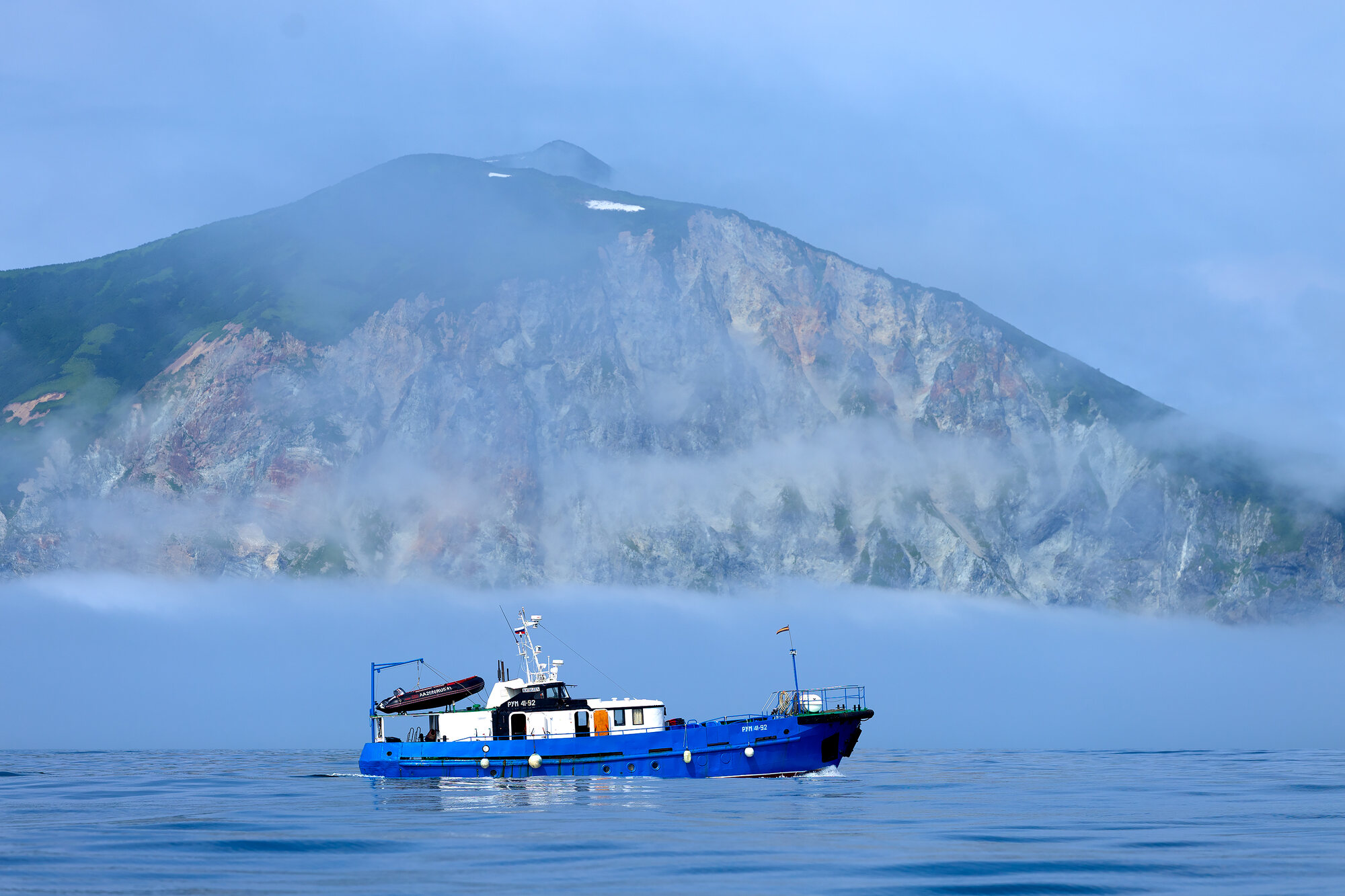 Our expedition boat on Avacha Bay, Kamchatka, below cliffs wrapped in sea mist