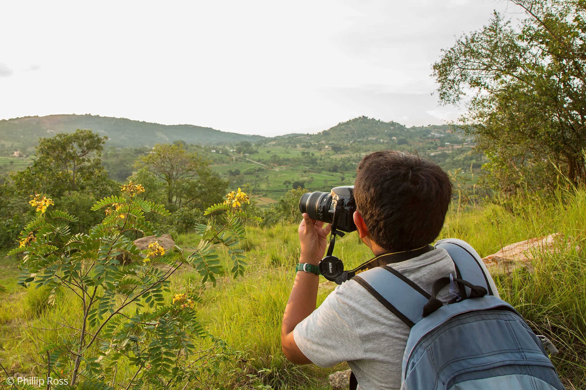 A young participant seen from behind, camera raised, photographing the landscape from a viewpoint on a Kids Photography Workshop
