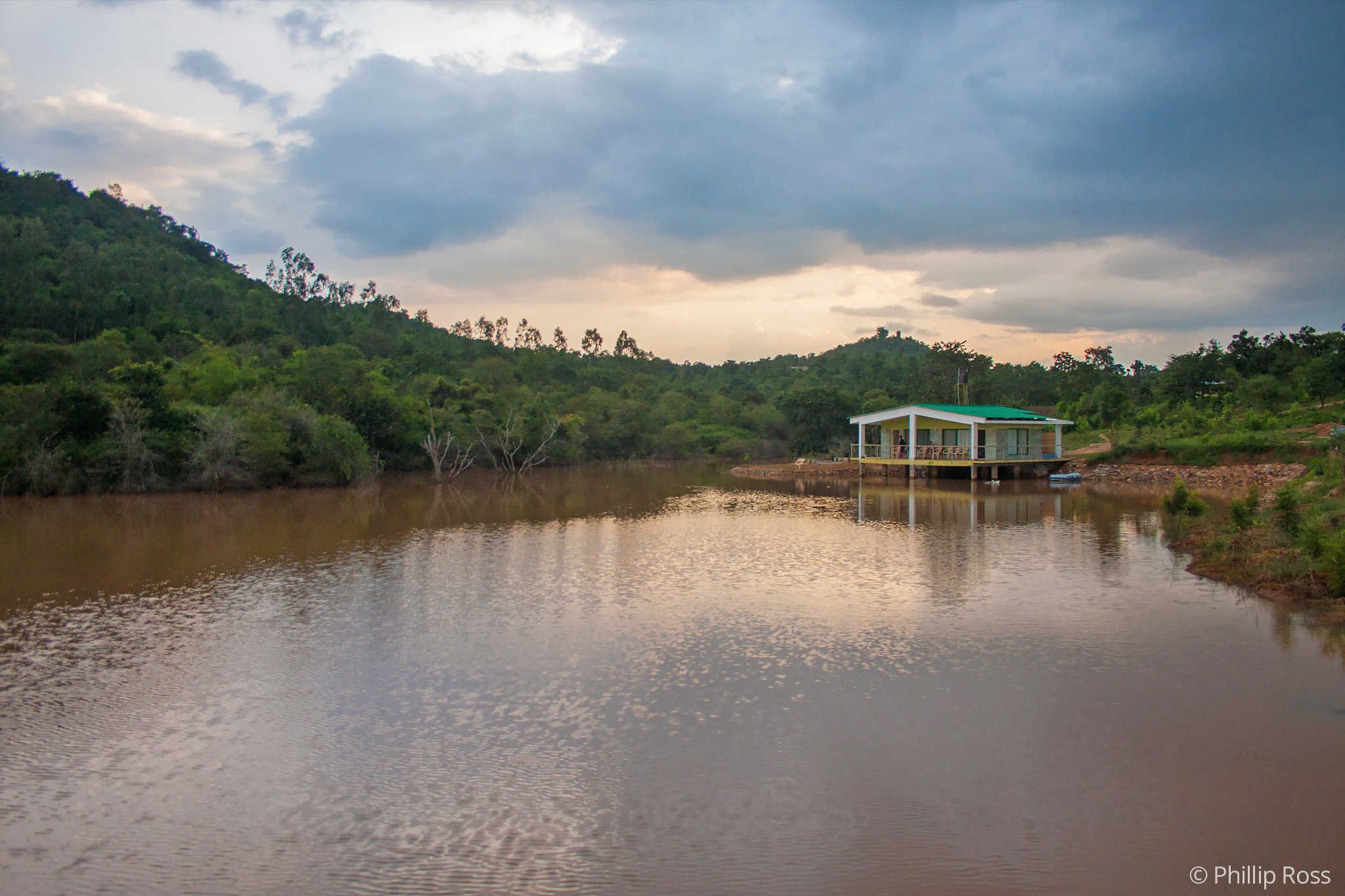 The Outback Farm and Homestay seen across its lake, with forested hills behind