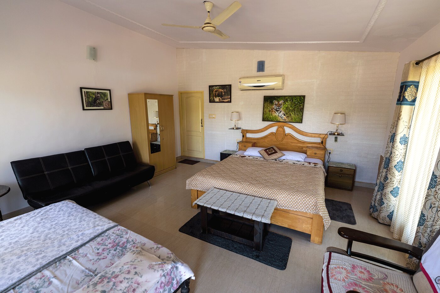 A luxury guest room with a king-size bed, a sofa, an extra bed and framed wildlife photographs on the walls